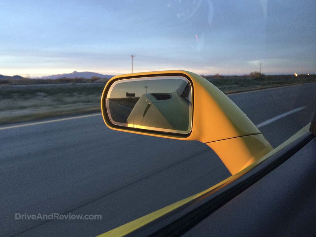 2015 yellow C7 Corvette side view mirror while driving on the freeway at sunset