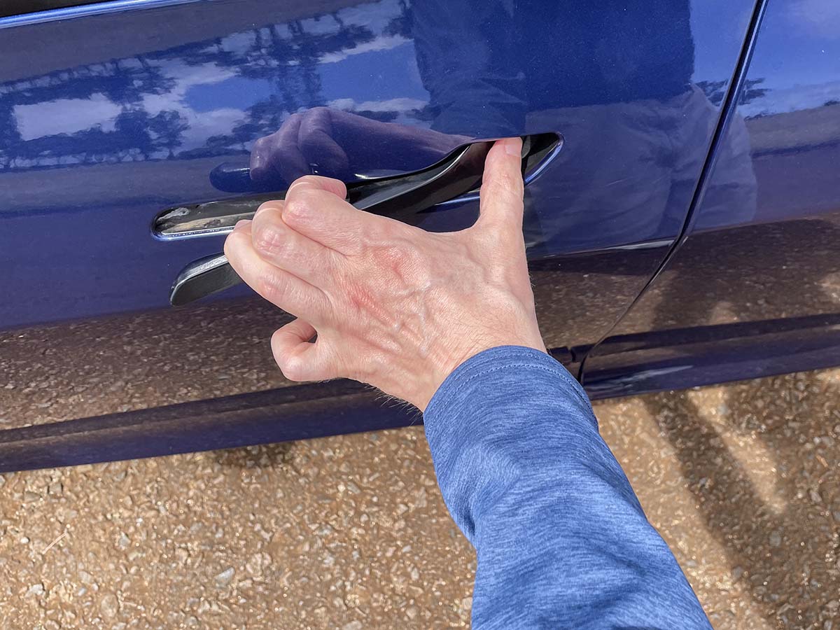Awkwardly trying to open the door of a Tesla model 3 but not knowing how to grab the door handle