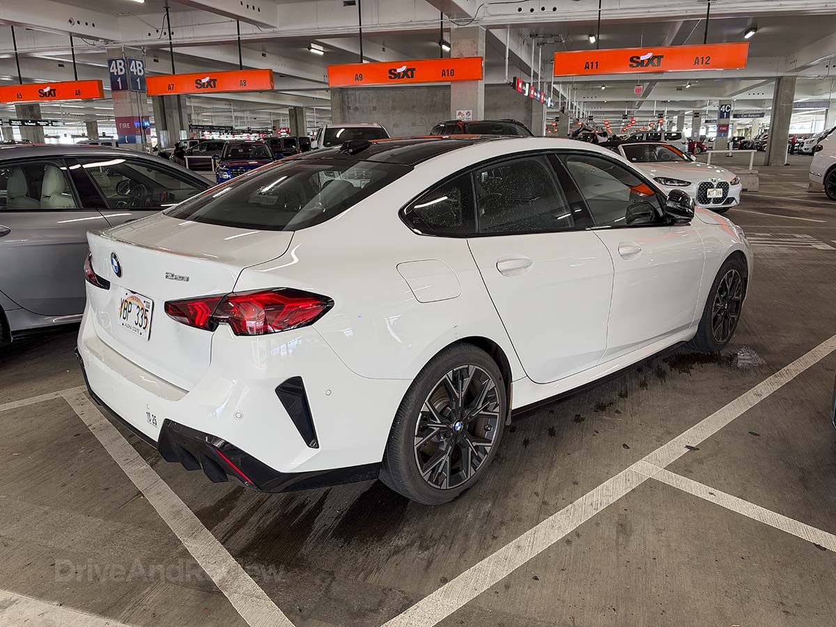 Rear 3/4 view of a white 2026 BMW 228 xDrive parked at the Sixt rental car garage Honolulu airport
